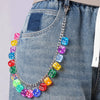 A silver chain necklace with colorful dice charms is clipped onto a denim jean pocket.