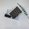A brown geometric print passport wallet is displayed next to a white card and a green leafy branch.