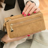 A close-up of a tan leather wallet with a gold zipper and multiple card slots being held by a person wearing a white blazer.