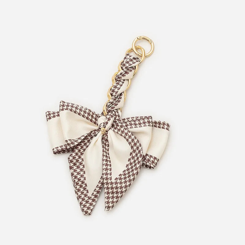 A beige and brown checkered fabric bow with a gold chain strap extension for a handbag.