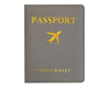 A gray PU leather passport holder with gold foil printing of an airplane and the word PASSPORT.