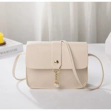 A beige fashion square crossbody bag with gold hardware resting on a white surface.