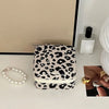 A leopard print PU leather jewelry storage box is displayed on a white surface next to some gold rings and a white candle.
