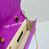 A close-up view of a purple clutch bag featuring high-end fabrics and gold hardware.