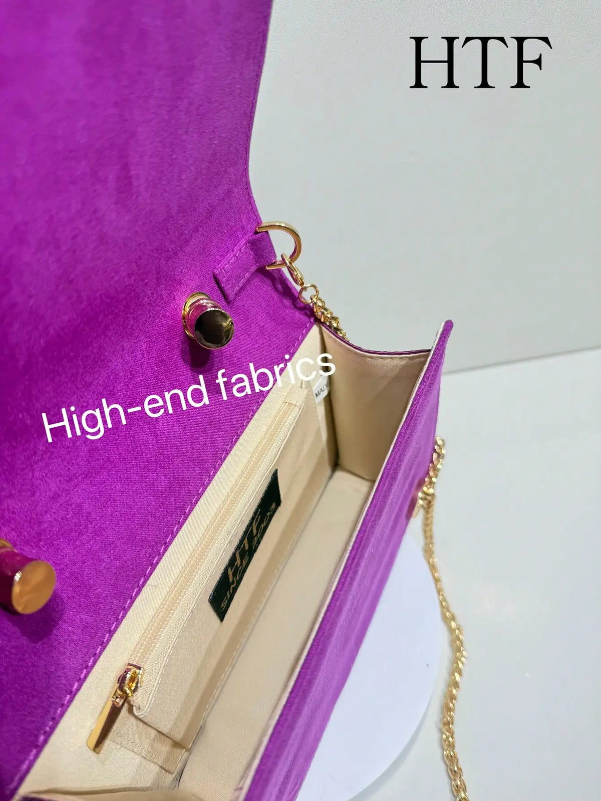 A close-up view of a purple clutch bag featuring high-end fabrics and gold hardware.