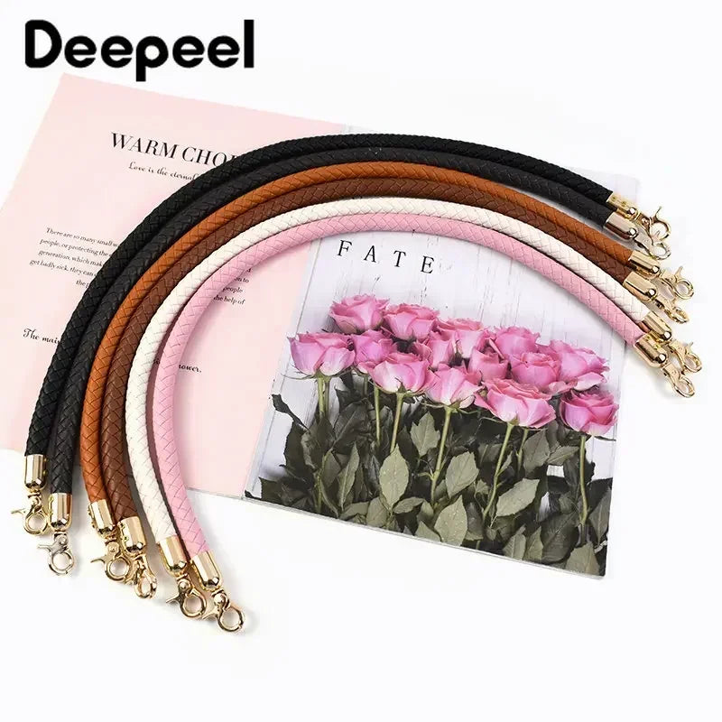A set of interchangeable leather bag handles in shades of brown, black, and pink are displayed on a pink background.