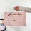 A hand is holding a pink PU laptop sleeve with a leather-look flap and gold-toned hardware.