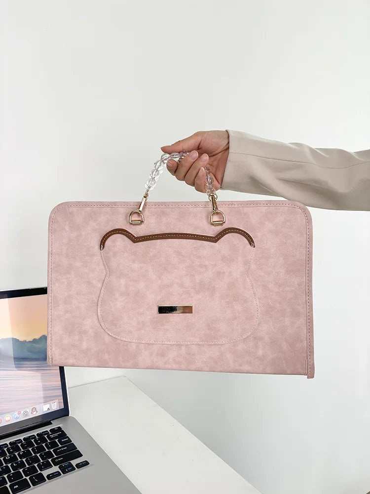 A hand is holding a pink PU laptop sleeve with a leather-look flap and gold-toned hardware.