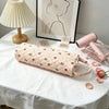 A quilted beige storage bag for hair dryer and personal items resting on a white tablecloth next to a pink hair dryer.