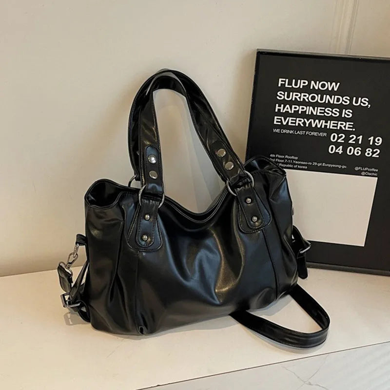 A black leather shoulder bag with a strap is displayed on a white surface.