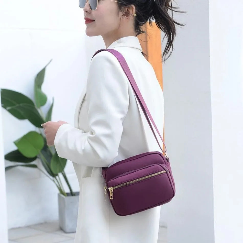 A woman wearing a white coat and purple crossbody bag standing indoors.