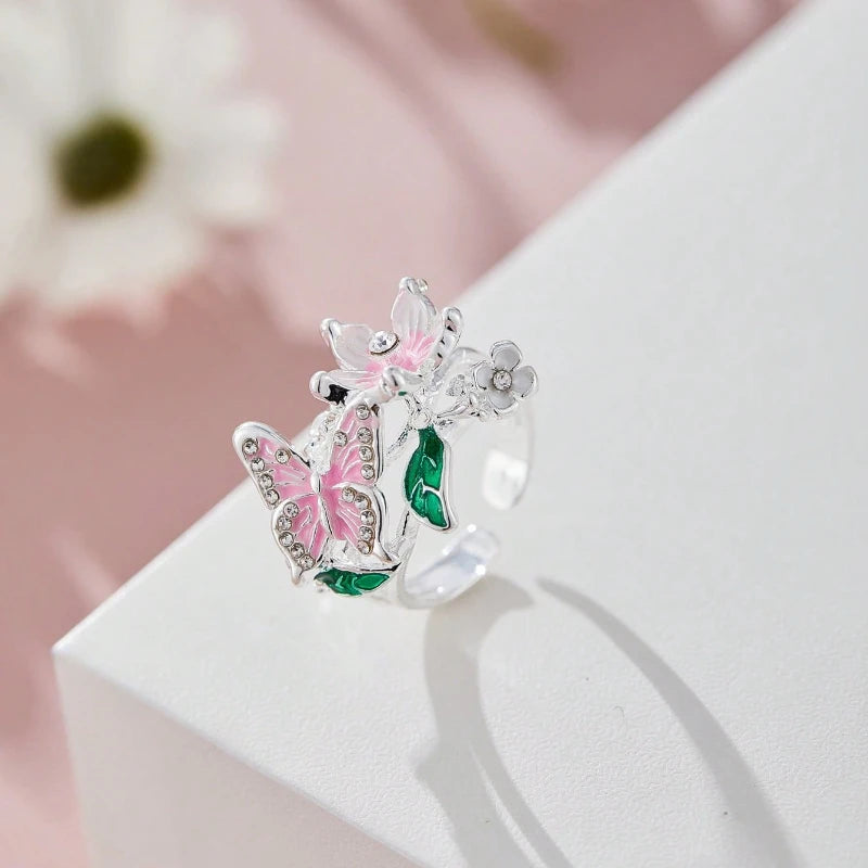 Silver butterfly rings featuring pink and green enamel flowers displayed on a white surface.