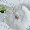 A white lace bow keychain with pearl strands and a silver heart pendant resting on a white surface.