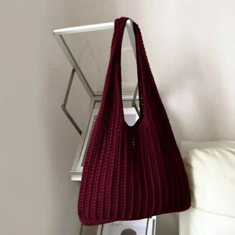 A deep burgundy knit shoulder bag hanging on a white display rack.