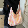 A light pink and yellow striped canvas shoulder bag is held by a person wearing a black shirt.
