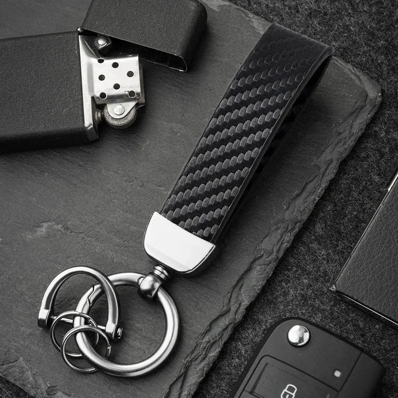 A close-up shot of a carbon fiber leather keychain attached to a black surface.