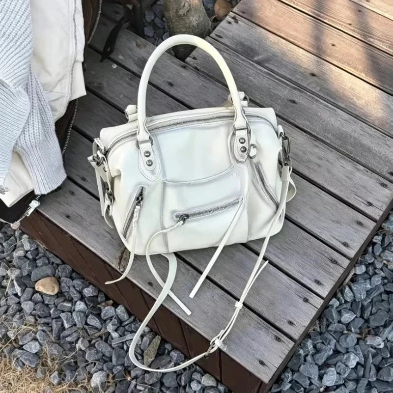 A white retro motorcycle PU leather crossbody shoulder bag resting on a wooden surface.