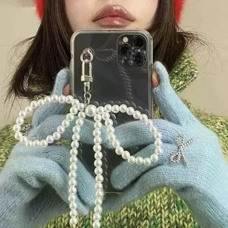 A hand holds a pearl bow keychain with a heart pendant against a blurred background.