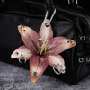 A realistic pink and purple orchid flower keychain attached to a black leather handbag.