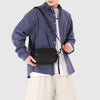 A person wearing a blue plaid shirt and white top holds a black PU leather crossbody bag.