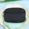 Black nylon mini coin purse with a double zipper for holding cards and ID placed on a light green plate.
