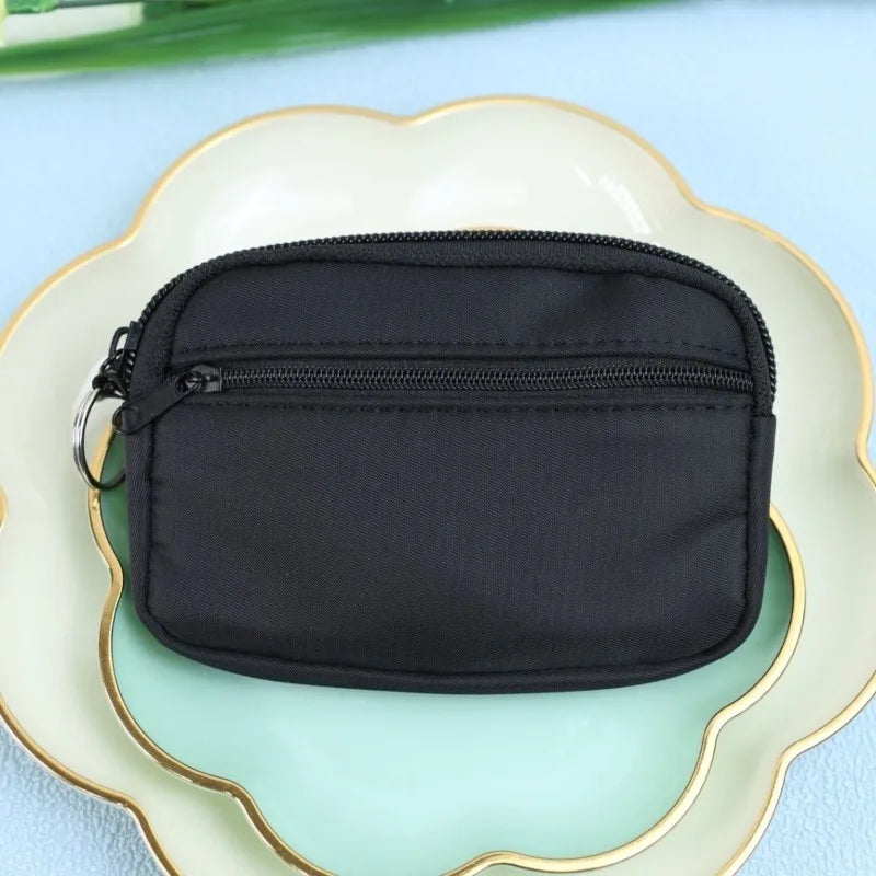 Black nylon mini coin purse with a double zipper for holding cards and ID placed on a light green plate.
