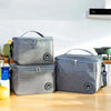Two gray insulated lunch tote bags resting on a wooden counter with a yellow fruit.