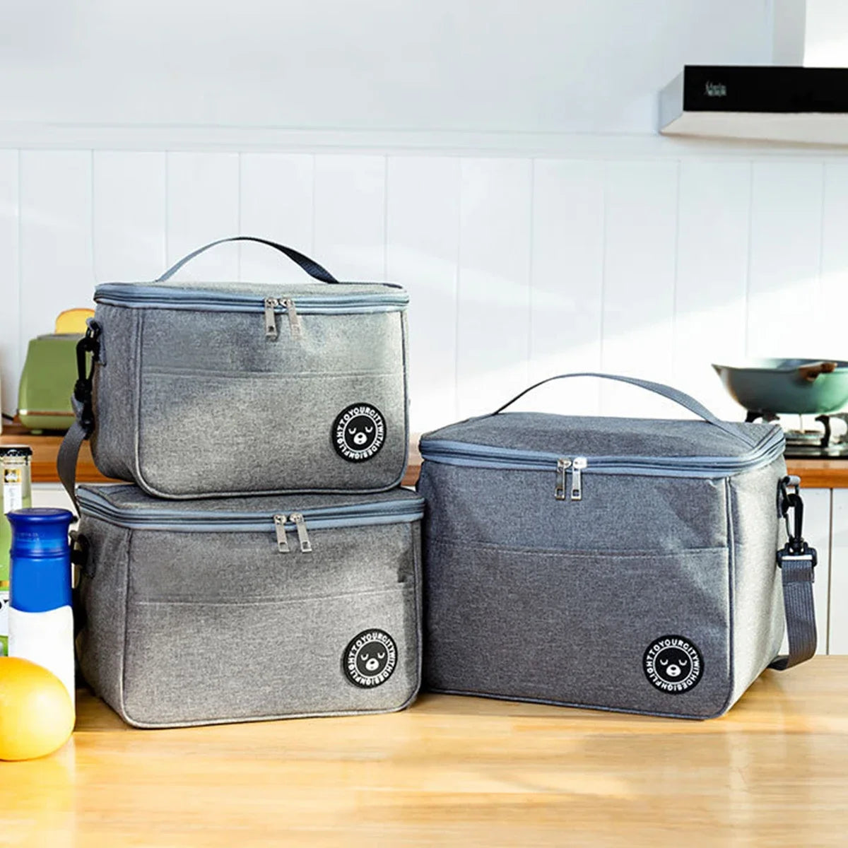Two gray insulated lunch tote bags resting on a wooden counter with a yellow fruit.