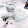 A light blue quilted cotton makeup organizer set with a lid and a separate pouch, displayed on a white marble surface.