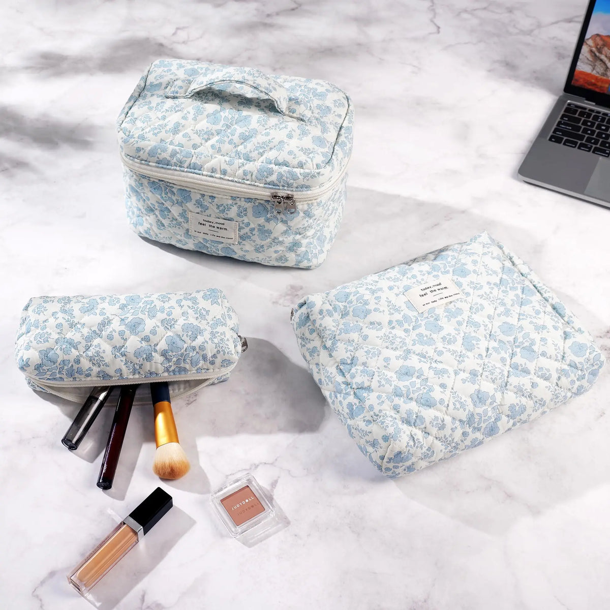 A light blue quilted cotton makeup organizer set with a lid and a separate pouch, displayed on a white marble surface.