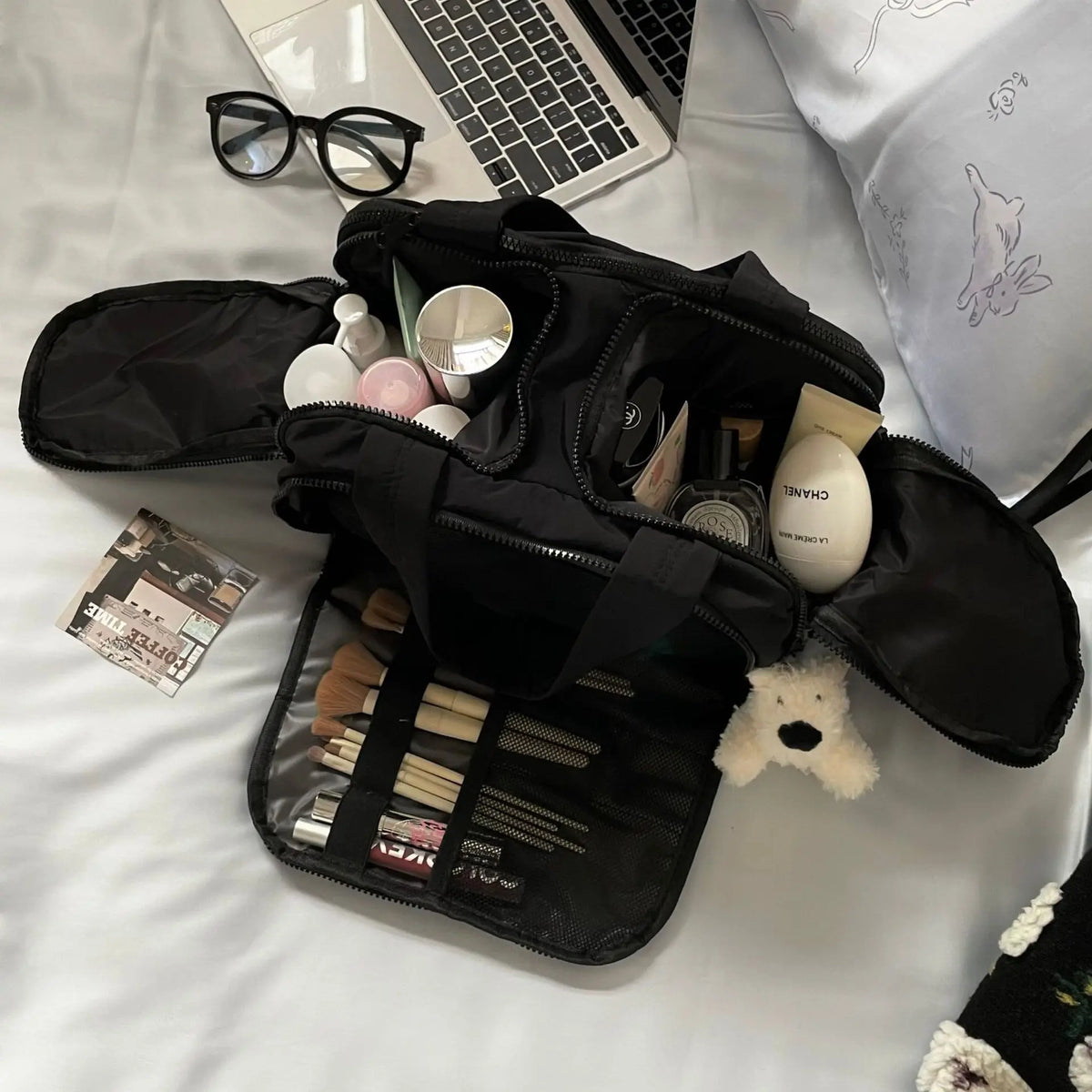 Schwarze, luxuriöse portable Make-up-Organizer-Tasche, geöffnet auf weißer Fläche mit verschiedenen Pinsel- und Produkten