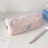 Eine pinke Polka-Dot-Pencilcase neben einem rosa Bleistift und einem blauen Buch