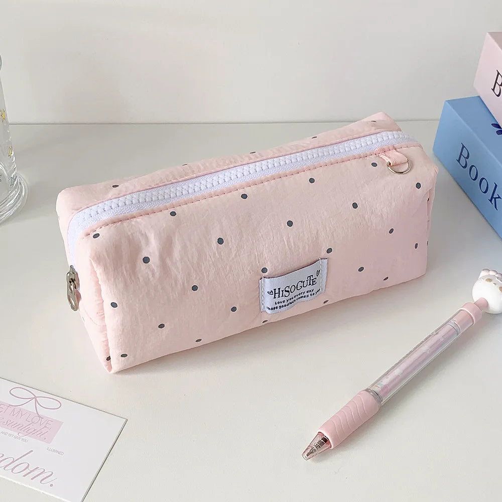 Eine pinke Polka-Dot-Pencilcase neben einem rosa Bleistift und einem blauen Buch