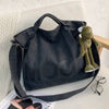 A dark gray canvas tote bag featuring a large letter design and a small green stuffed animal resting on it.