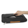 A hand is opening a black multi-pocket laptop sleeve with a handle.
