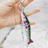A hand holds a colorful fish-themed acrylic keychain charm with iridescent scales and blue accents.