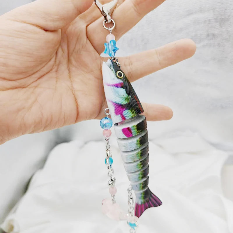 A hand holds a colorful fish-themed acrylic keychain charm with iridescent scales and blue accents.