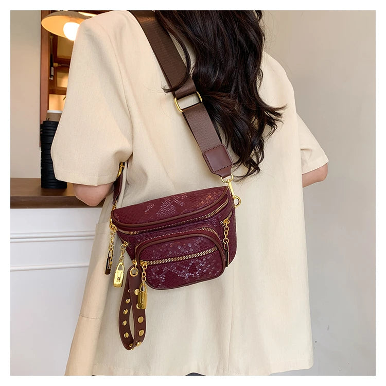 A woman is wearing a maroon Rivet waist bag crossbody fanny pack with gold hardware under a light beige jacket.