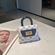 A white and black floral textured crossbody bag with a dark leather flap and gold hardware resting on a white marble surface.