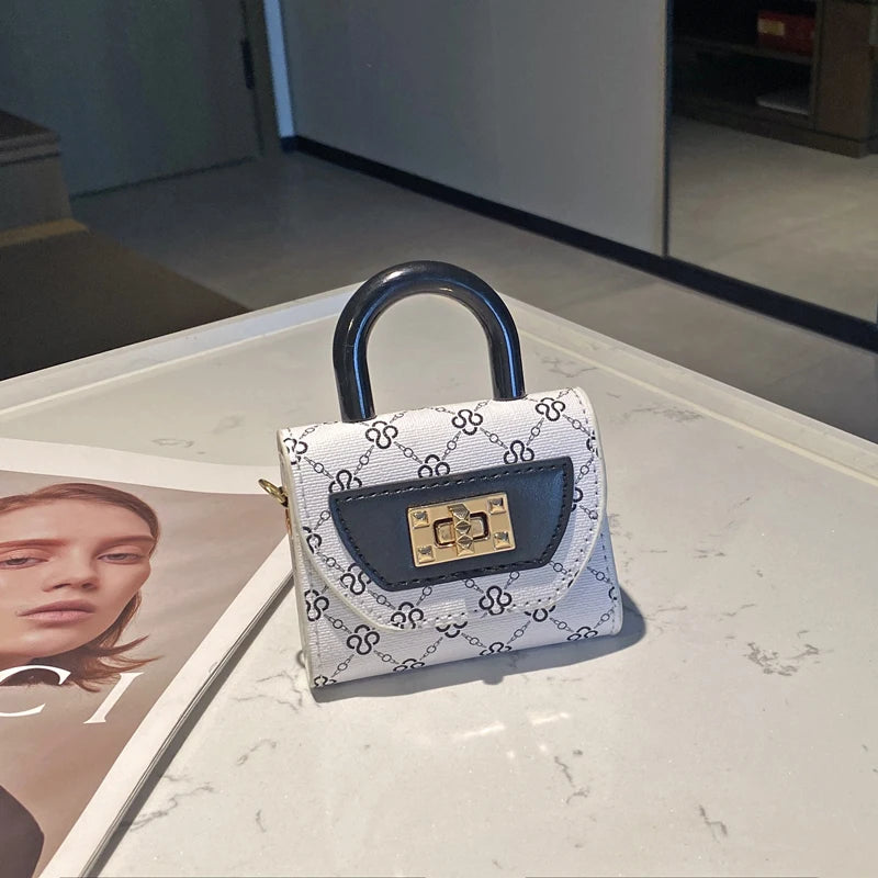 Bolso cruz floral blanco y negro con solapa de cuero oscuro y herrajes dorados sobre una superficie de mármol blanco.