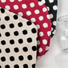 A close-up of a fabric featuring red and white polka dots, displayed next to a clear glass.