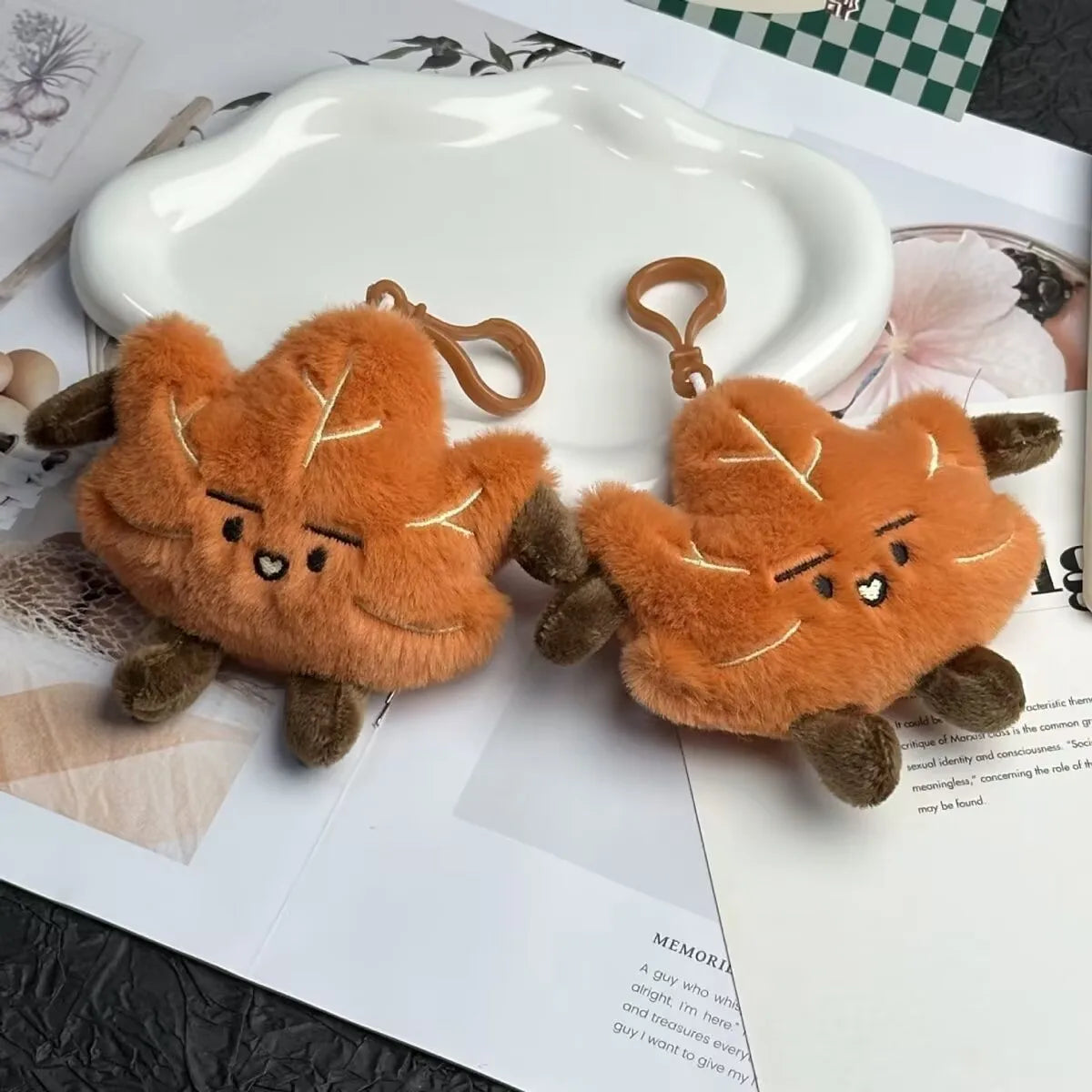 An orange maple leaf plush keychain charm resting on a white ceramic plate.