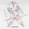 A white floral patterned nylon bag strap with a gold buckle is displayed on a wooden surface.