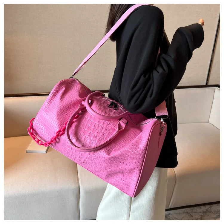 A woman holds a bright pink crocodile grain PU leather travel duffle bag against a light background.