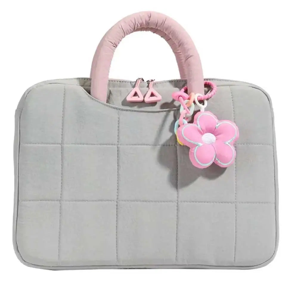 A light gray quilted laptop sleeve with a pink fabric handle and decorative flower charms.