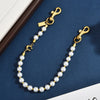 A gold chain necklace with white pearls and a letter charm accessory displayed on a dark blue background.