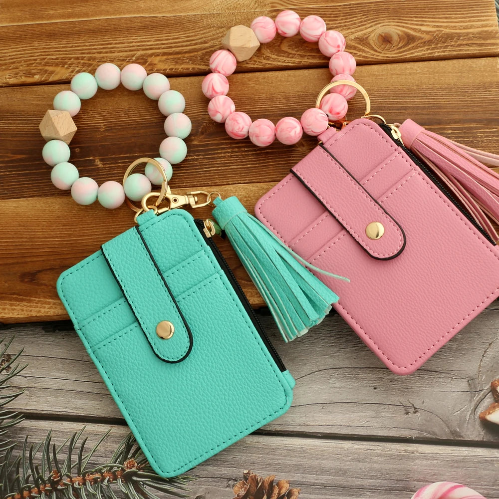 A pink and mint silicone PU leather key chain wristlet wallet with beaded bracelets on a wooden surface.
