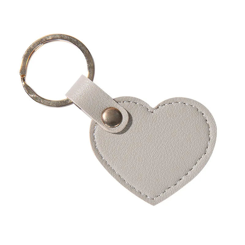A small, light gray leather heart-shaped keychain with a metal ring and clasp.