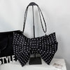 Black pleated bow crossbody tote bag displayed on a stand against a white background.
