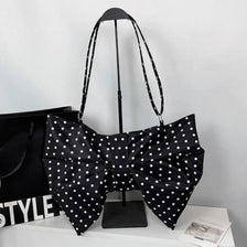 Black pleated bow crossbody tote bag displayed on a stand against a white background.